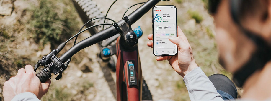 Fietser met rode mountainbike die voorzien is van een Bosch System Controller en Mini Remote terwijl hij de e-bike Flow app op zijn telefoon in de hand heeft