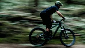 Fietser rijd met zijn mountainbike hard door het bos waardoor de omgeving donker en onscherp is