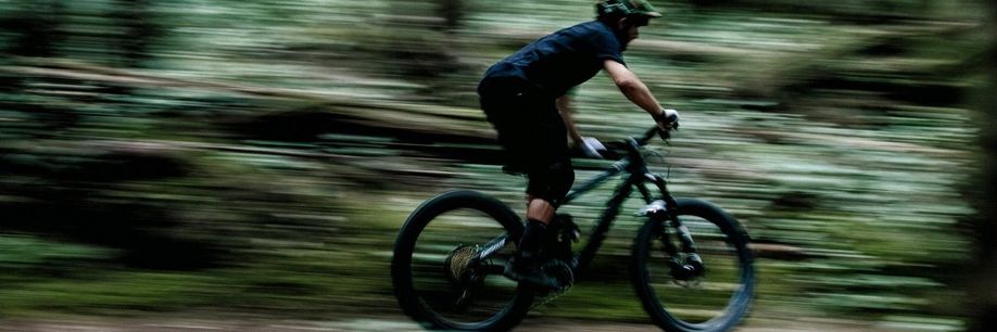Fietser rijd met zijn mountainbike hard door het bos waardoor de omgeving donker en onscherp is