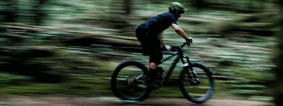 Fietser rijd met zijn mountainbike hard door het bos waardoor de omgeving donker en onscherp is