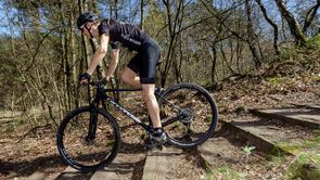 Fietser in 12GO Biking fietsshirt daalt met zwarte cannondale mountainbike af van een houten trap in het bos
