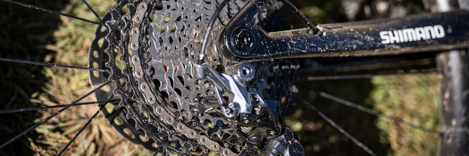 Shimano cassette en achterderailleur op een zwarte mountainbike met Shimano sticker op het frame met gras op de achtergrond