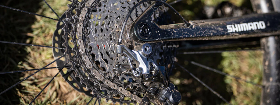 Shimano cassette en achterderailleur op een zwarte mountainbike met Shimano sticker op het frame met gras op de achtergrond