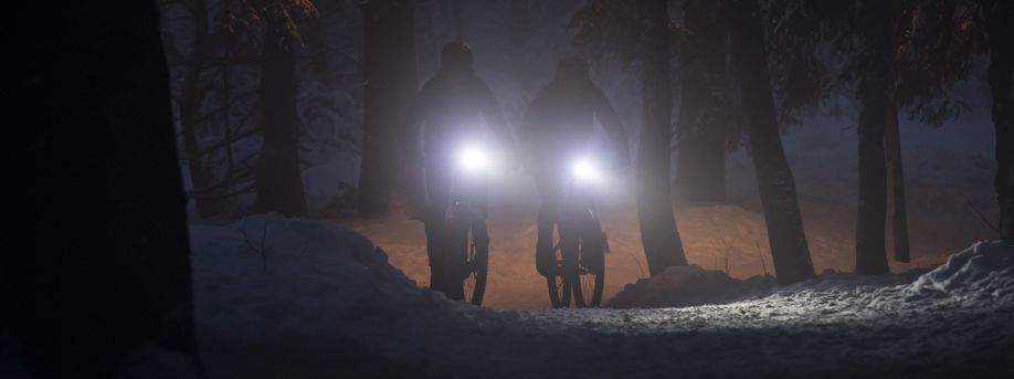 Twee fietsers in een zeer donker bos met felle voorlichten die de witte sneeuw belichten