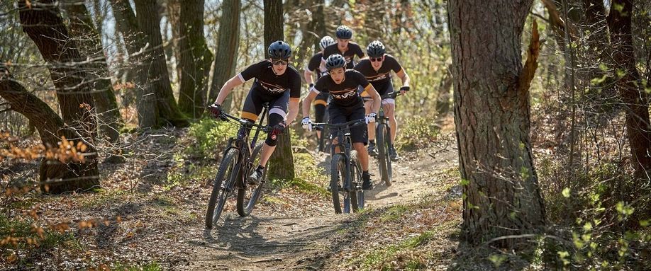 Groep van 12GO Biking fietsers die op mountainbikes achter elkaar over een bospad door de kale bomen