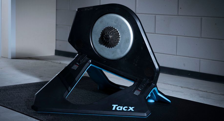 Tacx Neo 2T fietstrainer op een zwarte Tacx trainermat voor een betongetegelde muur