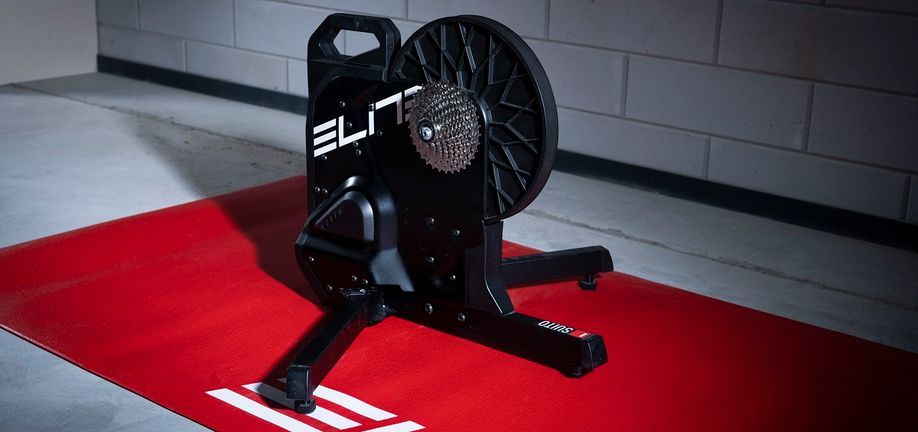Elite Suito-T fietstrainer op een rode Elite trainermat voor een betonnen getegelde muur