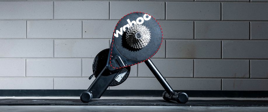 Uitlichting van het vliegwiel van een Wahoo Kickr Core fietstrainer op een zwarte Wahoo trainermat met betongetegelde muur als achtergrond