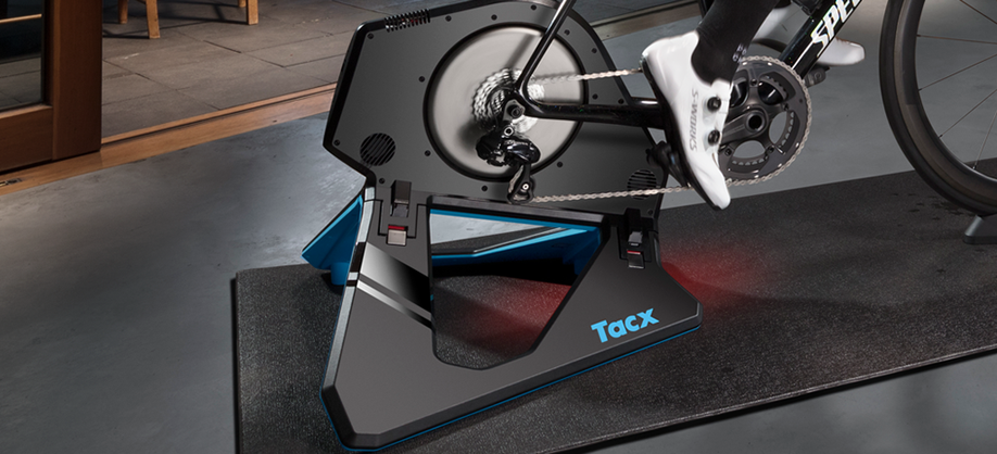 Tacx Neo 2T wordt gebruikt op een zwarte trainermat met een betonnen grijze vloer en een houten rand met openslaande deuren achter