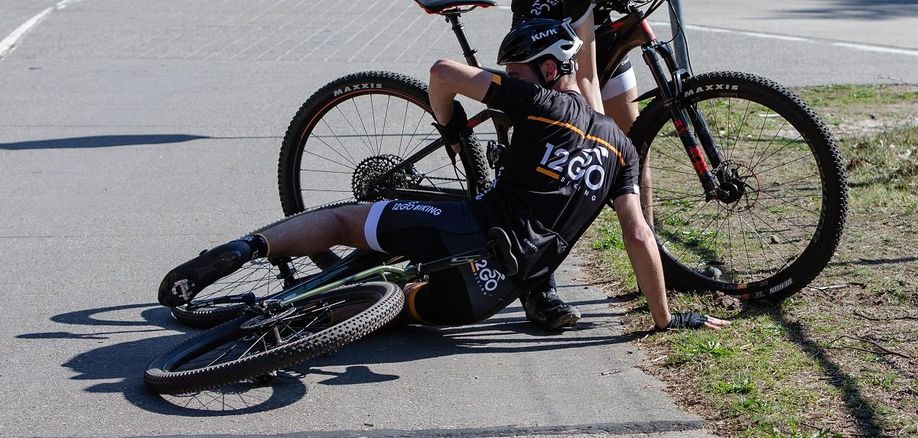 Fietser met 12GO Biking fietskleding onderuit op het asfalt met een groene mountainbike