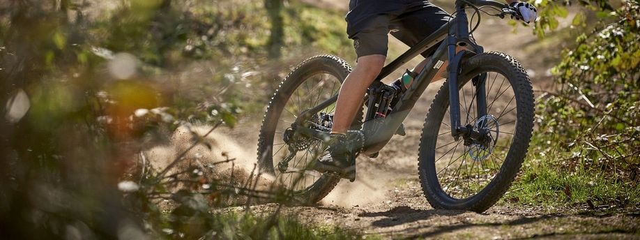 Fietser met full suspension Trek mountainbike slipt over grondpad tussen de struiken door