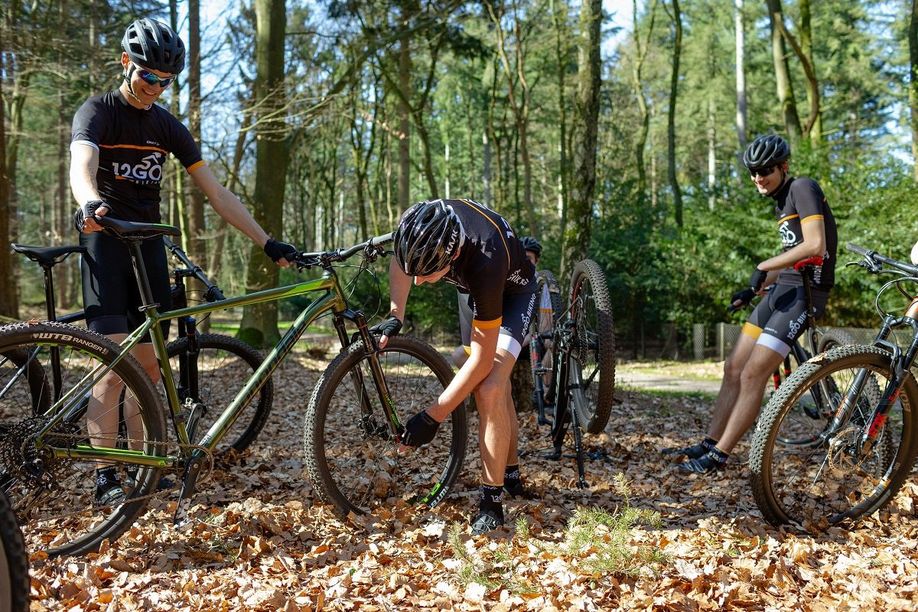 Groep mountainbikers met 12GO fietskleding lopen hun mountainbikes na in bos met veel bladeren
