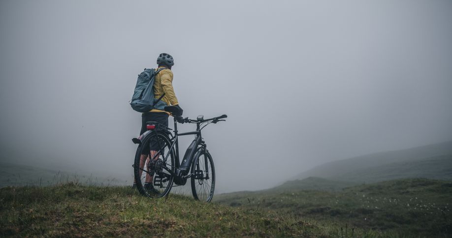 Man met elektrische hybride fiets in de mist van de bergen op groen gras