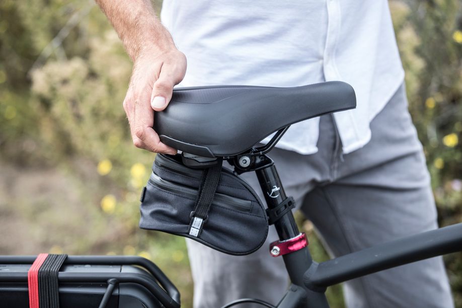 Man houdt fietszadel van Gazelle fiets aan de achterkant vast, waarbij er ook nog een kleine zadeltas onder het zadel zit