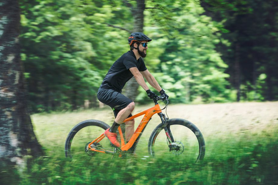 Man op oranje elektrische mountainbike Cube door groen landschap met bomen en veel hoog gras