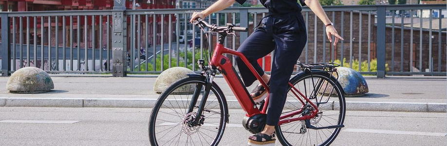 Vrouw met sandalen op Kalkhoff Endeavour slaat linksaf door arm uit te steken met halve stenen bollen en hek op achtergrond