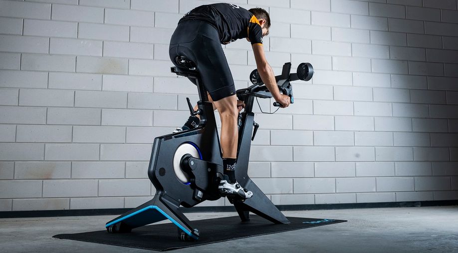 Man met 12GO Biking fietskleding op complete Tacx smartbike met Tacx trainermat voor een betonnen getegelde muur