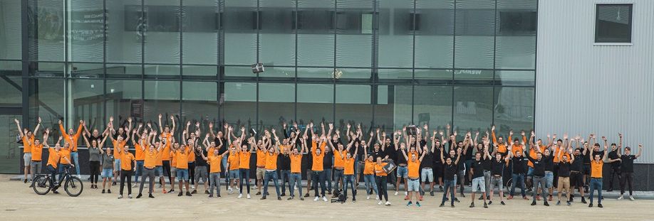 Grote groep 12GO Biking medewerkers voor nieuw pand met handen omhoog