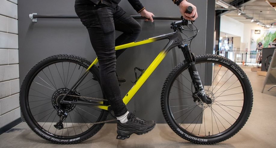 Fietser zit stil op mountainbike met rechterhiel op het pedaal onder en houd stuur en wand vast voor balans in de winkel