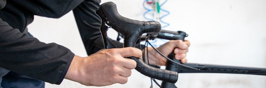 Persoon knijpt rem van racefiets in en test met zijn ander hand bij het balhoofd of er speling is