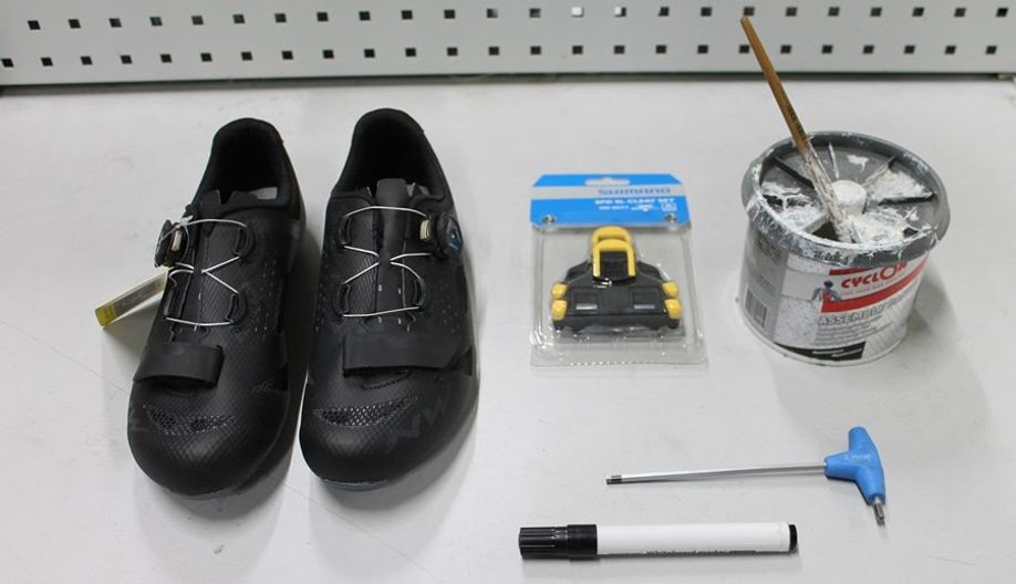 Racefietsschoenen, schoenplaatjes, inbus, stift en montagepasta op een werkbank om te laten zien wat je nodig hebt om schoenplaatjes correct te monteren