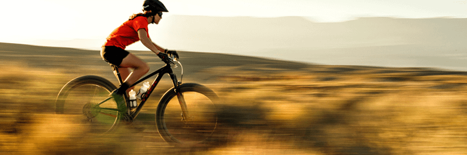 Vrouwelijke fietser met zwarte MTB die op snelheid over een heuvel fiets met veel gedroogd gras langs de kanten