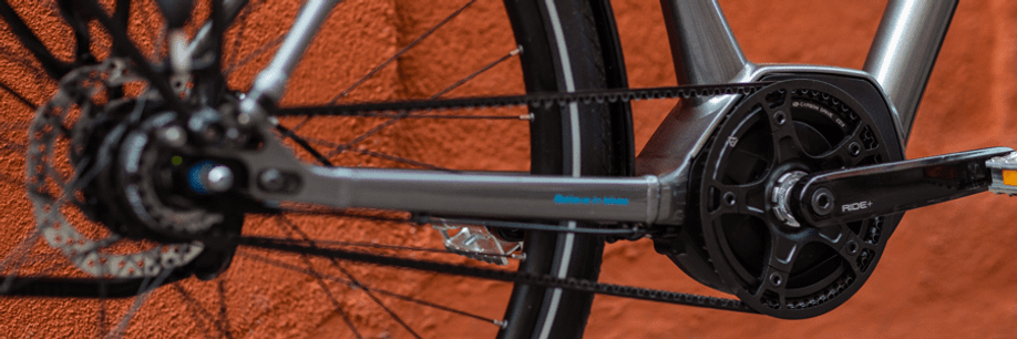 Elektrische fiets met grijs frame heeft middenmotor en riemaandrijving voor een rode muur