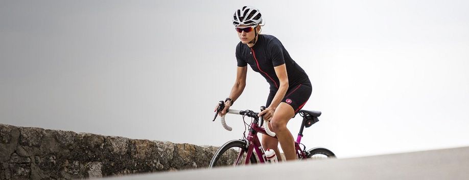 Vrouwelijke fietser met Castelli fietskleding en roze racefiets is aan het klimmen voor een stenen muurtje