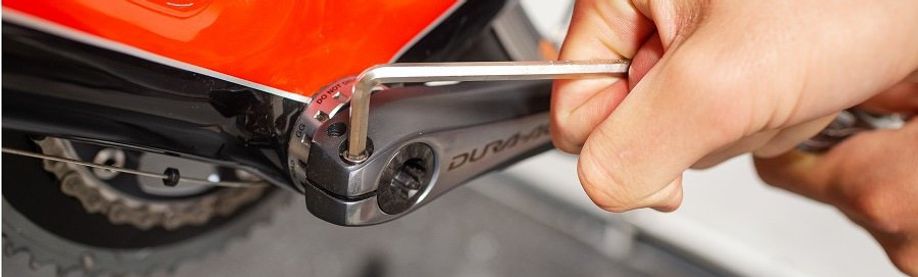 Persoon draait een Dura-Ace crankarm van een racefiets af met behulp van een inbussleutel
