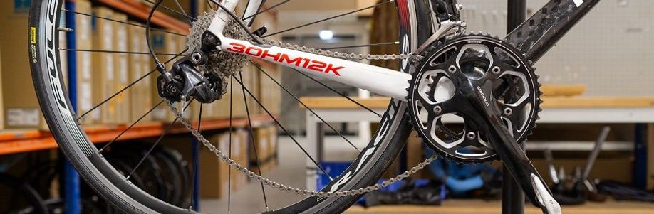 Ketting van een racefiets hangt los doordat dat van de het voorblad gehaald is met dozen fietsen en een werkbank op de achtergrond