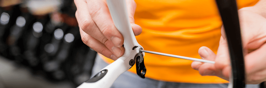 Man met oranje shirt draait derailleurpad los met behulp van een lange inbussleutel