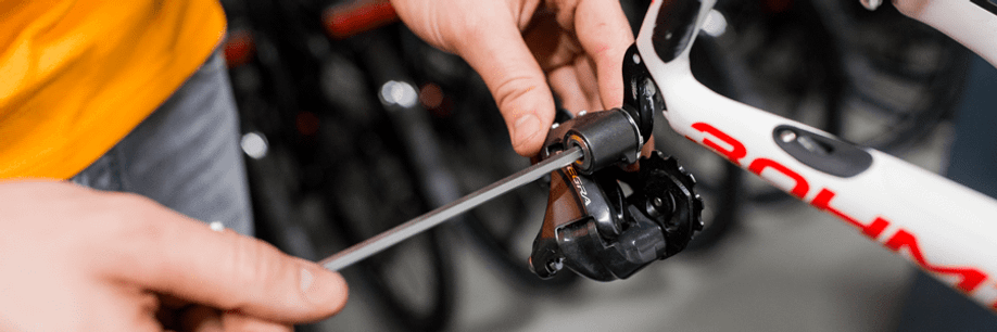 Man met oranje shirt monteert een Ultegra achterderailleur op een wit frame met behulp van een lange inbussleutel