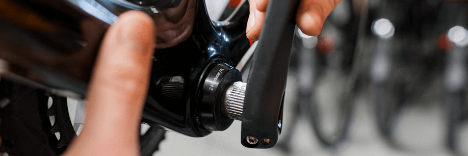 Persoon zet linker crankarm weer terug op de racefiets met wit en zwart frame