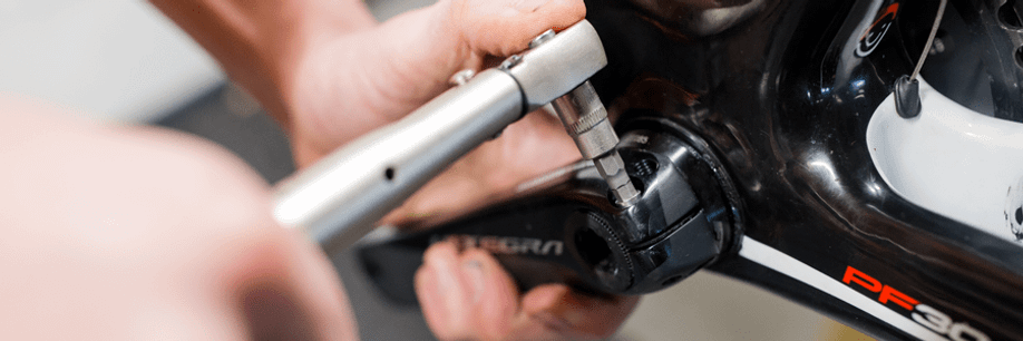 Persoon draait crankarmbouten weer aan met een momentsleutel voor het juiste aantal Nm