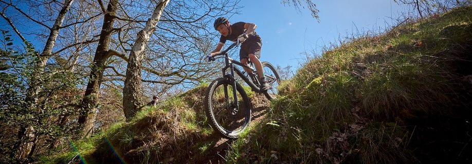 Mountainbiker met 12GO Fietsshirt die een steile afdeling neemt op een trail tussen de bomen door