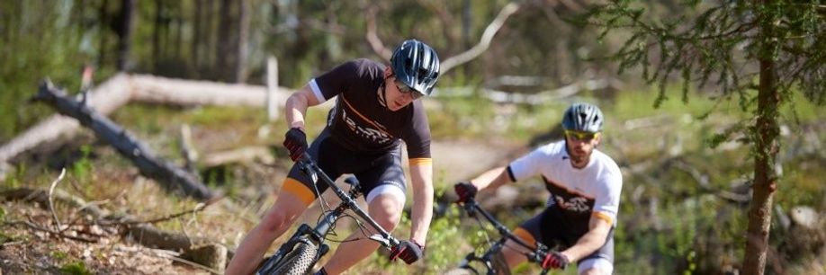 Twee mannelijke fietsers met 12GO Biking fietskleding rijden een trail door het bos met omgevallen bomen op de mountainbike