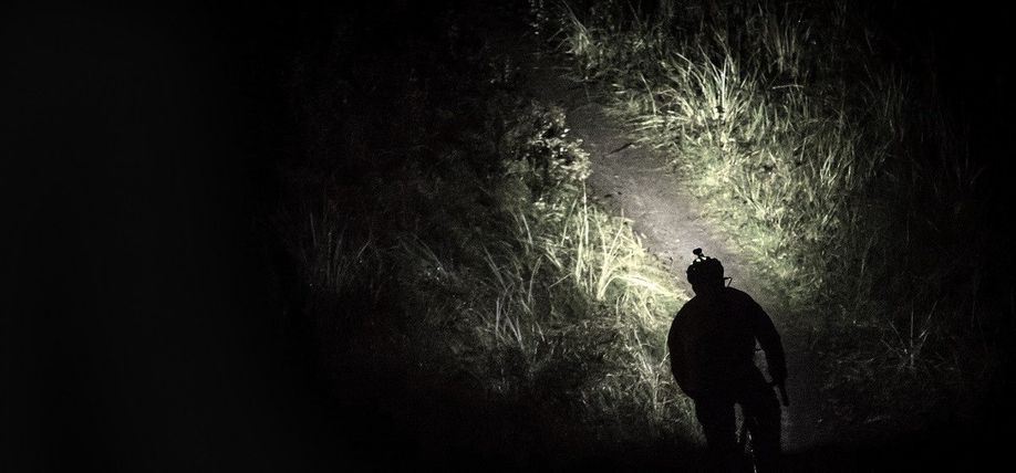 Mountainbiker die door het donker een trail pakt en alleen kan zien wat zijn felle voorlicht verlicht