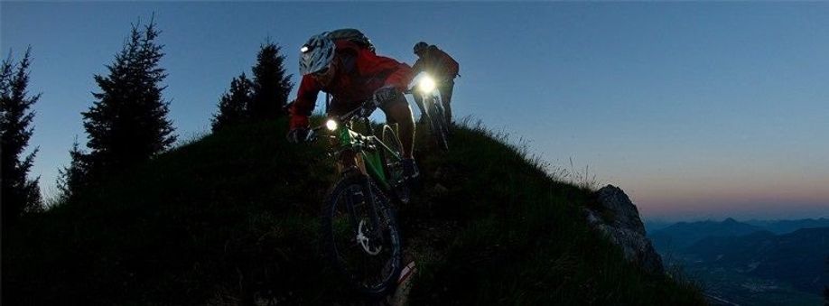 2 mountainbikers met felle voorlichten die van een berg af nightbiken