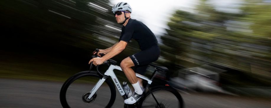 Man met zwarte fietskleding op wit met zwarte Scott Addict RC racefiets waarbij de achtergrond vervaagd is door de snelheid waarmee hij fietst