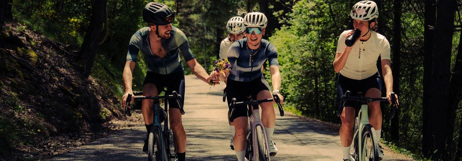 Groep racefietsers op Scott Addict fietsen waarbij een man wat kleine bloemen geeft aan een vrouw terwijl ze bergop fietsen
