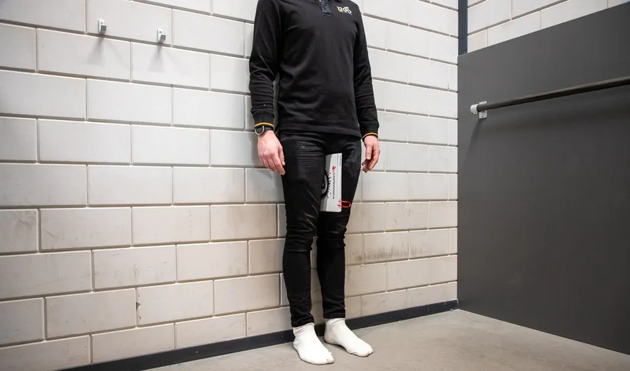 Persoon met rug tegen de muur en boek tussen de bovenbuin tegen het kruis om de binnenbeenlengte te bepalen