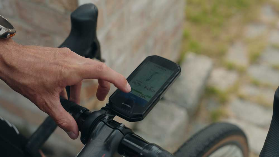 Garmin Edge 1050 op houder van racefietsstuur met een hand die de fietscomputer bediend