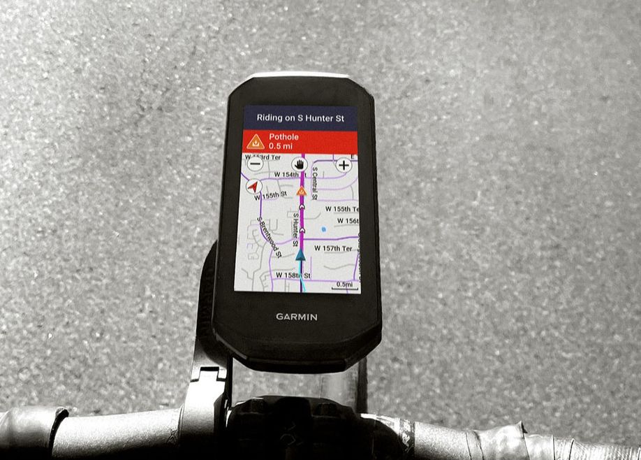 Garmin Edge 1050 op een zwart fietsstuur met houder en een navigatiescherm waarbij er een melding van een gat in de weg aangegeven wordt