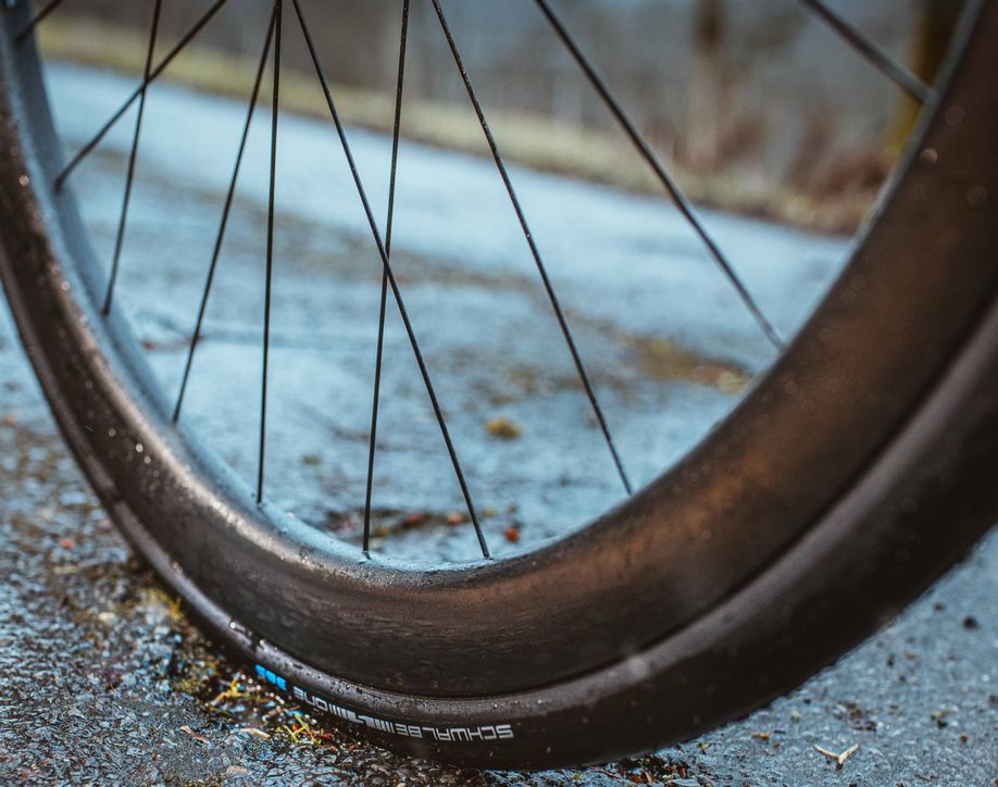 Close-up van een Schwalbe One 365 buitenband op een natte asfalt ondergrond langs de weg