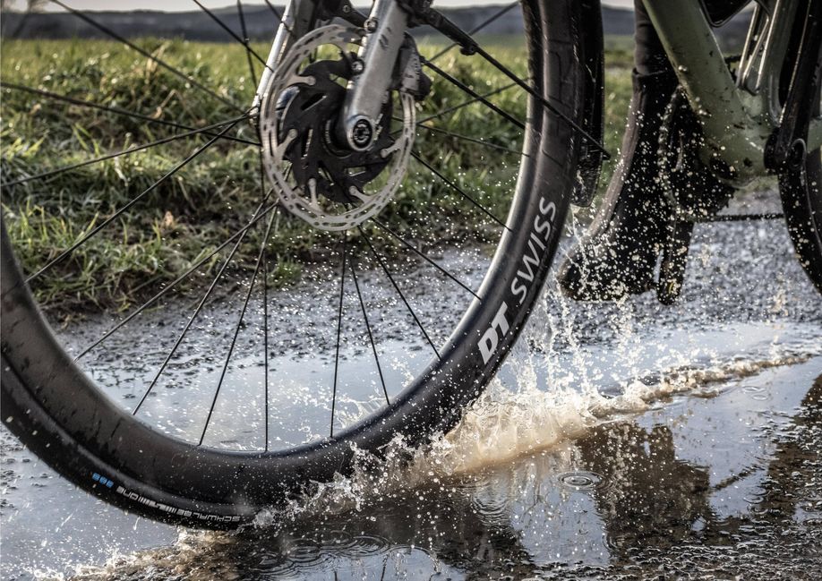 Wielrenner die op groene racefiets met DT Swiss velgen en Schwalbe One 365 banden door een plas op de weg fietst