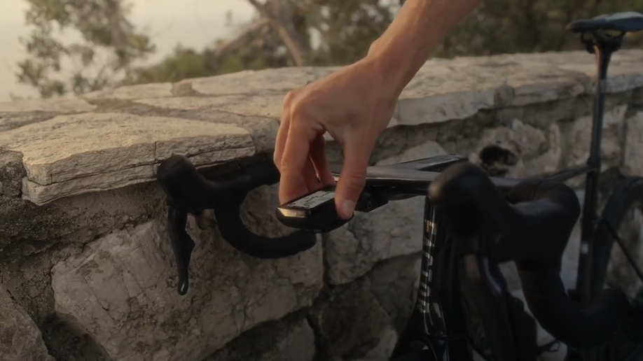 Hand die de Wahoo Elemnt Bolt 3 op een houder van een racefiets draait voor een stenen muur