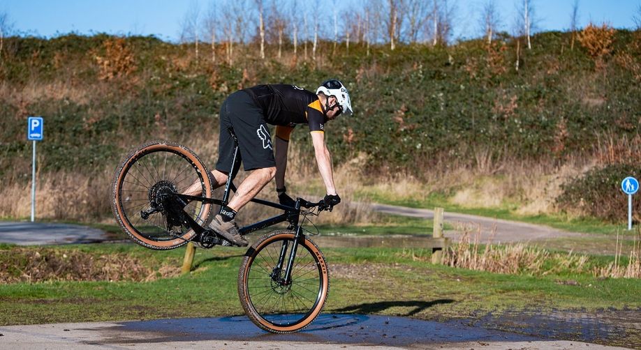 Mountainbiker met witte helm, 12GO Biking fietsshirt en Fox broek doet wheelie op voorband van zwarte mountainbike