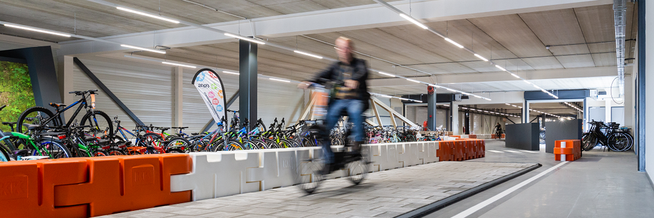 Fietser op 12GO Biking testbaan met tegels en rode met witte blokken als muurtje met veel kinderfietsen op achtergrond