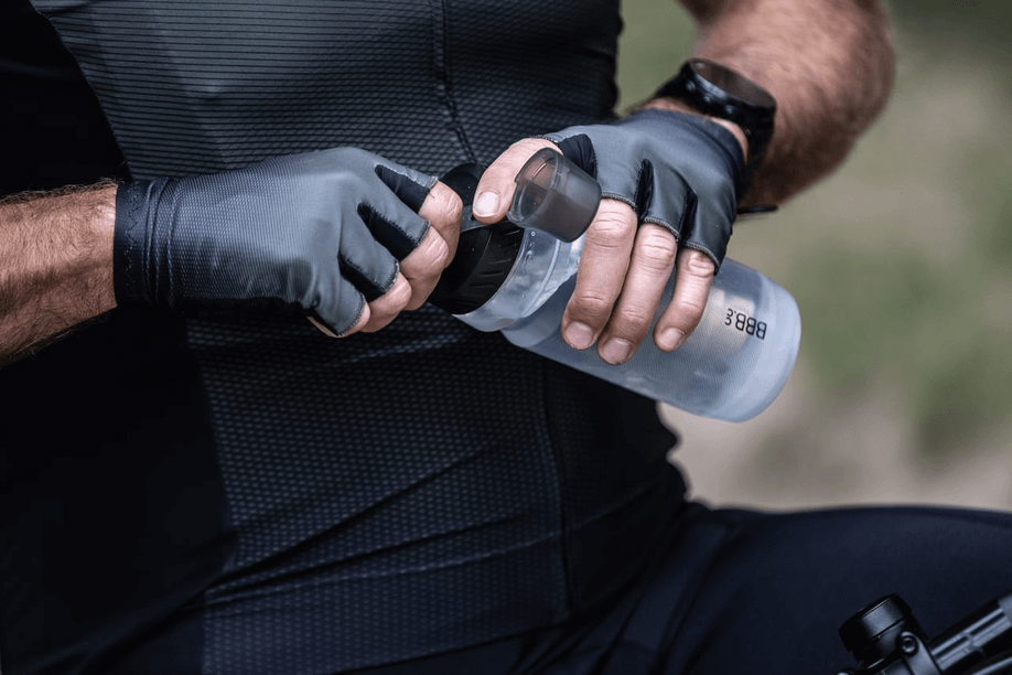 Man met zwart fietsshirt en handschoenen opent de tuit van een BBB bidon om zijn water te kunnen drinken