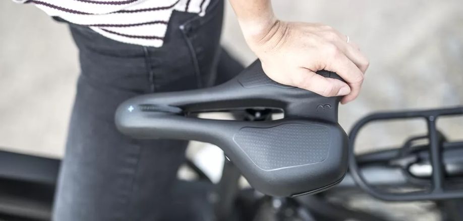 Vrouw staat bij zwarte fiets en duwt met een hand op het zwarte zadelvlak met uitsparing